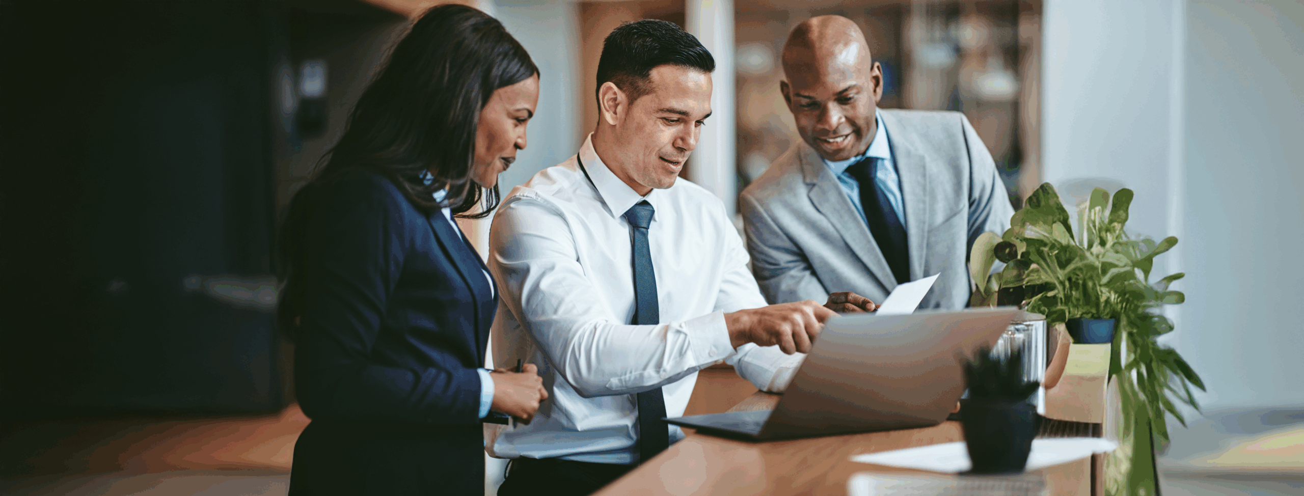 Diverse group of smiling businesspeople reading paperwork together while working on a laptop at a table in an office.